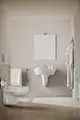 Weißes Wand-WC von Ideal Standard mit flachem, modernem Design. Handtuchhalter und Pflegeprodukte auf einem minimalistischen Waschbecken in einem hellen Badezimmer.